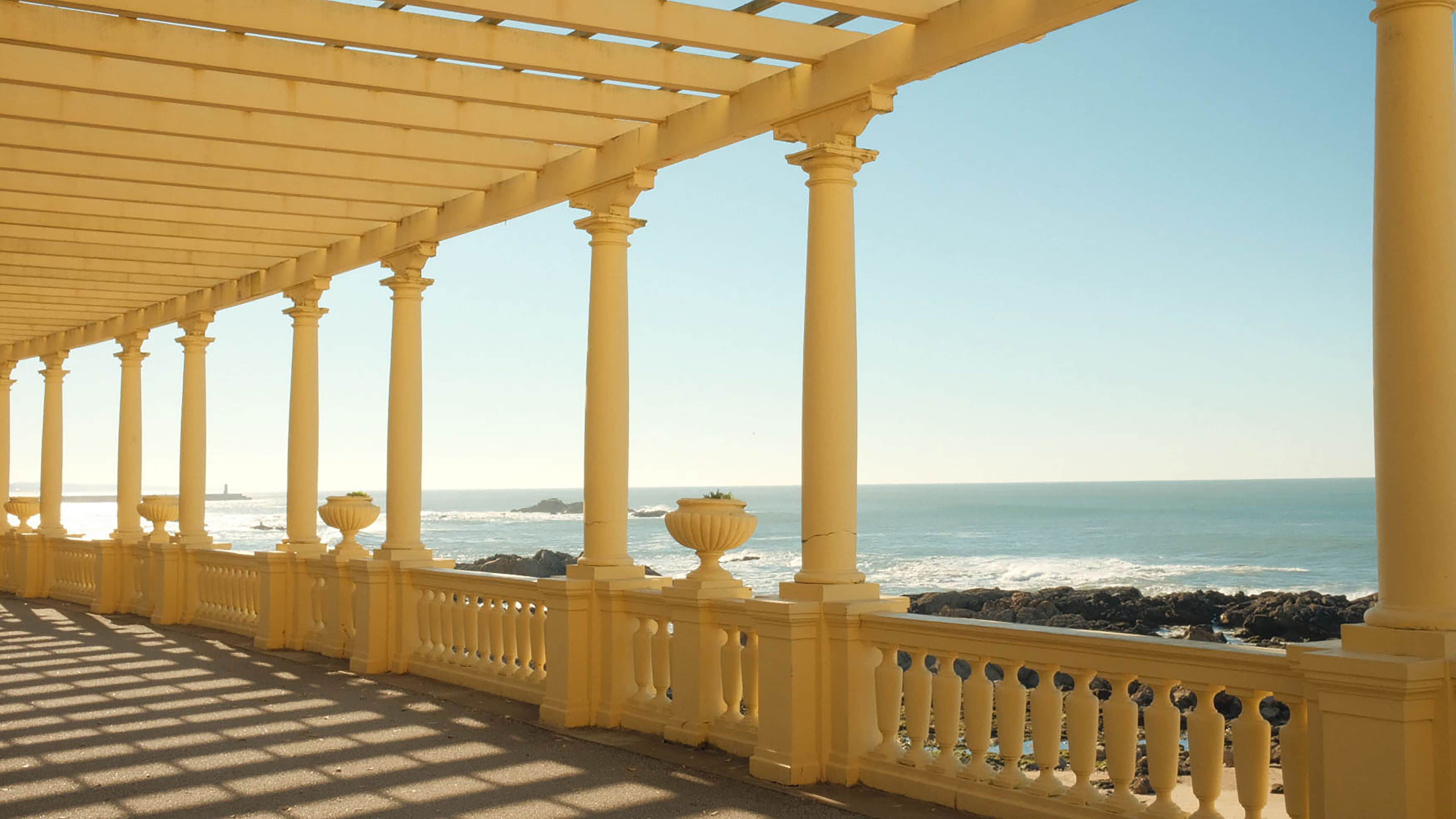 Une allée couverte, agrémentée de colonnes et de balustrades, qui offre une vue sur l’océan.