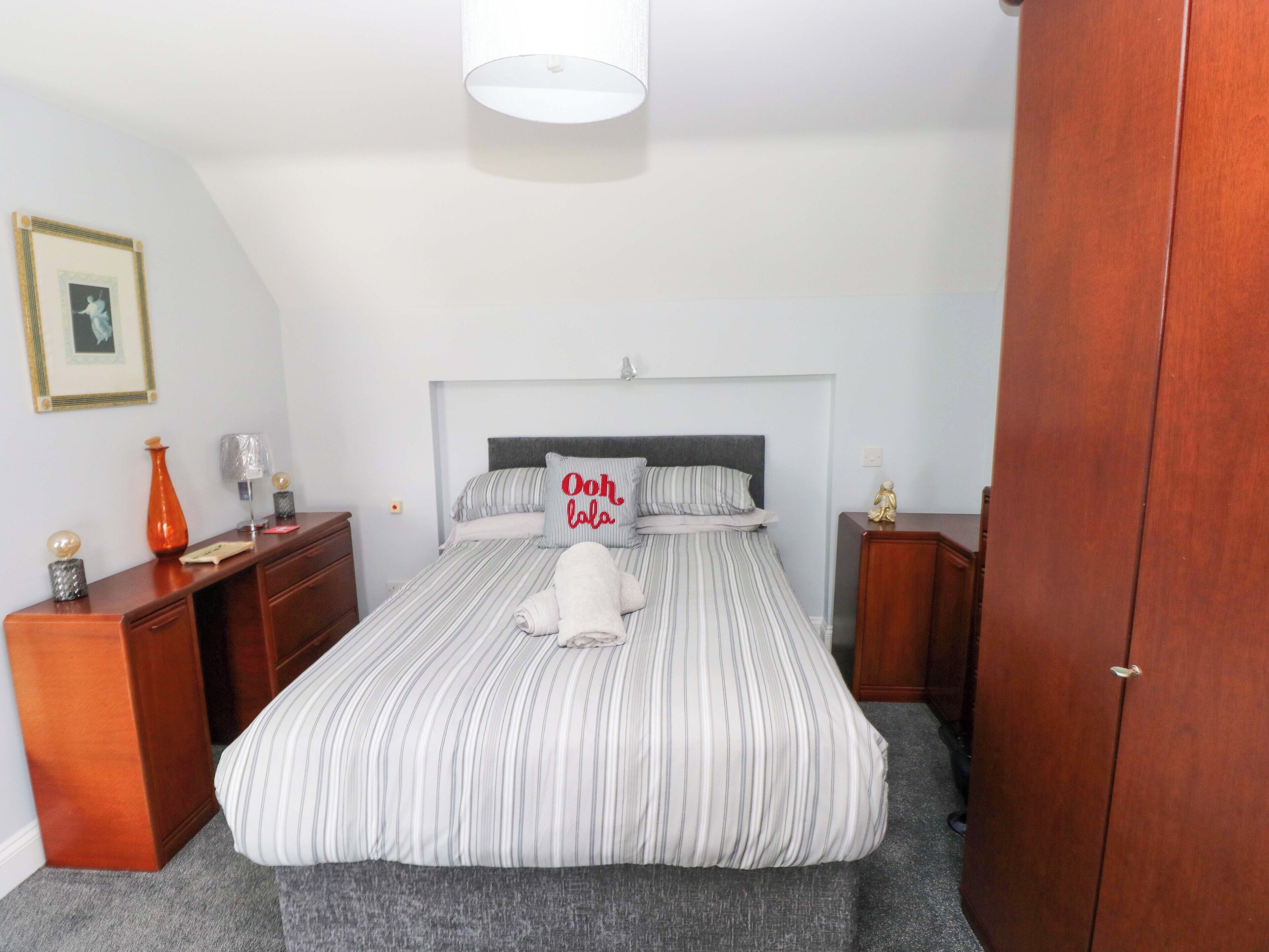 A bedroom with a bed, bedside tables, a dresser, a lamp, a framed picture, and a wardrobe.