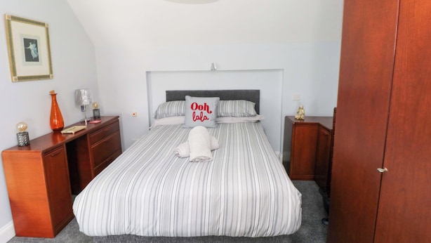 A bedroom with a bed, bedside tables, a dresser, a lamp, a framed picture, and a wardrobe. - Newgale Cottage (Haverfordwest)