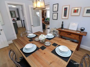 A dining room with a wooden table set for four, chairs, a vase with flowers, and framed pictures on the wall. - Newgale Cottage (Haverfordwest)