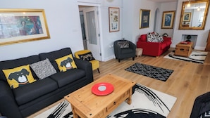 A living room with a black sofa, a wooden coffee table, a red plate, and a patterned rug. - Newgale Cottage (Haverfordwest)