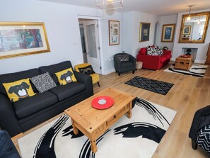 A living room with a black sofa, a wooden coffee table, a red plate, and a patterned rug. - Newgale Cottage (Haverfordwest)