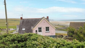 A pink house with a grey roof, a visible chimney, and a view of the beach. - Newgale Cottage (Haverfordwest)