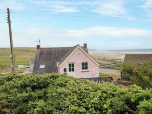 A pink house with a grey roof, a visible chimney, and a view of the beach. - Newgale Cottage (Haverfordwest)