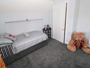 A single bed with striped bedding, a small bedside table with a lamp, and a teddy bear on the floor. - Newgale Cottage (Haverfordwest)
