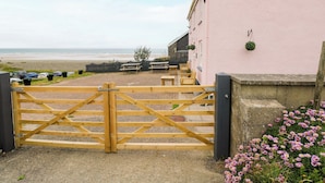 A coastal building with a wooden gate, outdoor seating, and a view of the beach. - Newgale Cottage (Haverfordwest)