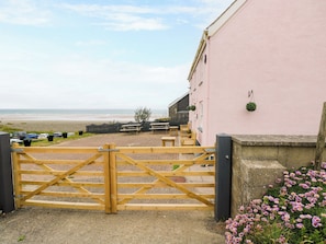 A coastal building with a wooden gate, outdoor seating, and a view of the beach. - Newgale Cottage (Haverfordwest)