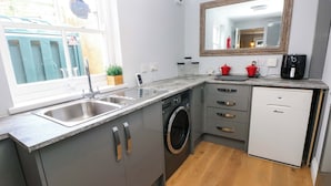 A compact kitchen with a washing machine, a sink, and a small refrigerator. - Newgale Cottage (Haverfordwest)