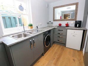 A compact kitchen with a washing machine, a sink, and a small refrigerator. - Newgale Cottage (Haverfordwest)