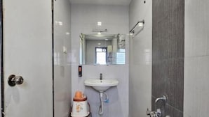 A narrow bathroom with a sink, mirror, and shower. - Hotel Royal Residency Executive  (Sangli Miraj Kupwad)