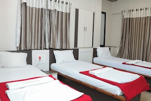 Habitació d'hotel amb tres llits individuals, cadascun amb llençol vermell i almoades blanques. Hi ha un armari amb mirall sobre els llits, i la habitació té una paleta de colors neutres.