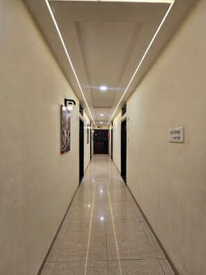 A long, well-lit hallway with a tiled floor, doors on both sides, and a sign on the right wall.