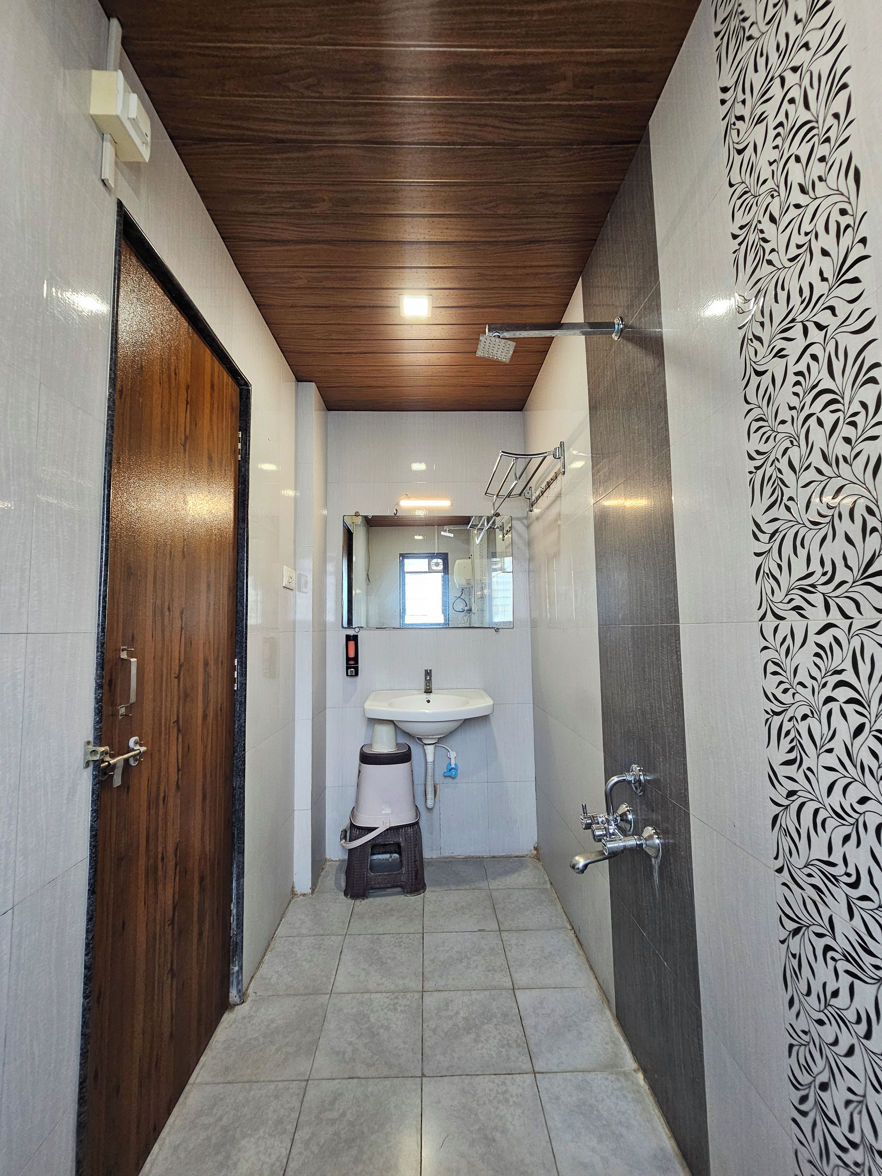 A narrow bathroom with a wooden door, a sink, and a shower.