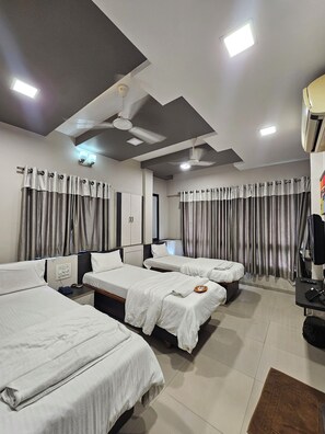 A hotel room with four single beds, a ceiling fan, recessed lighting, and a large window with curtains.