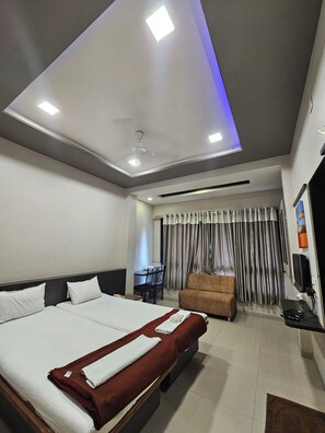 Quarto de hotel com uma cama grande, um sofá, uma escrivaninha com cadeira e uma televisão.