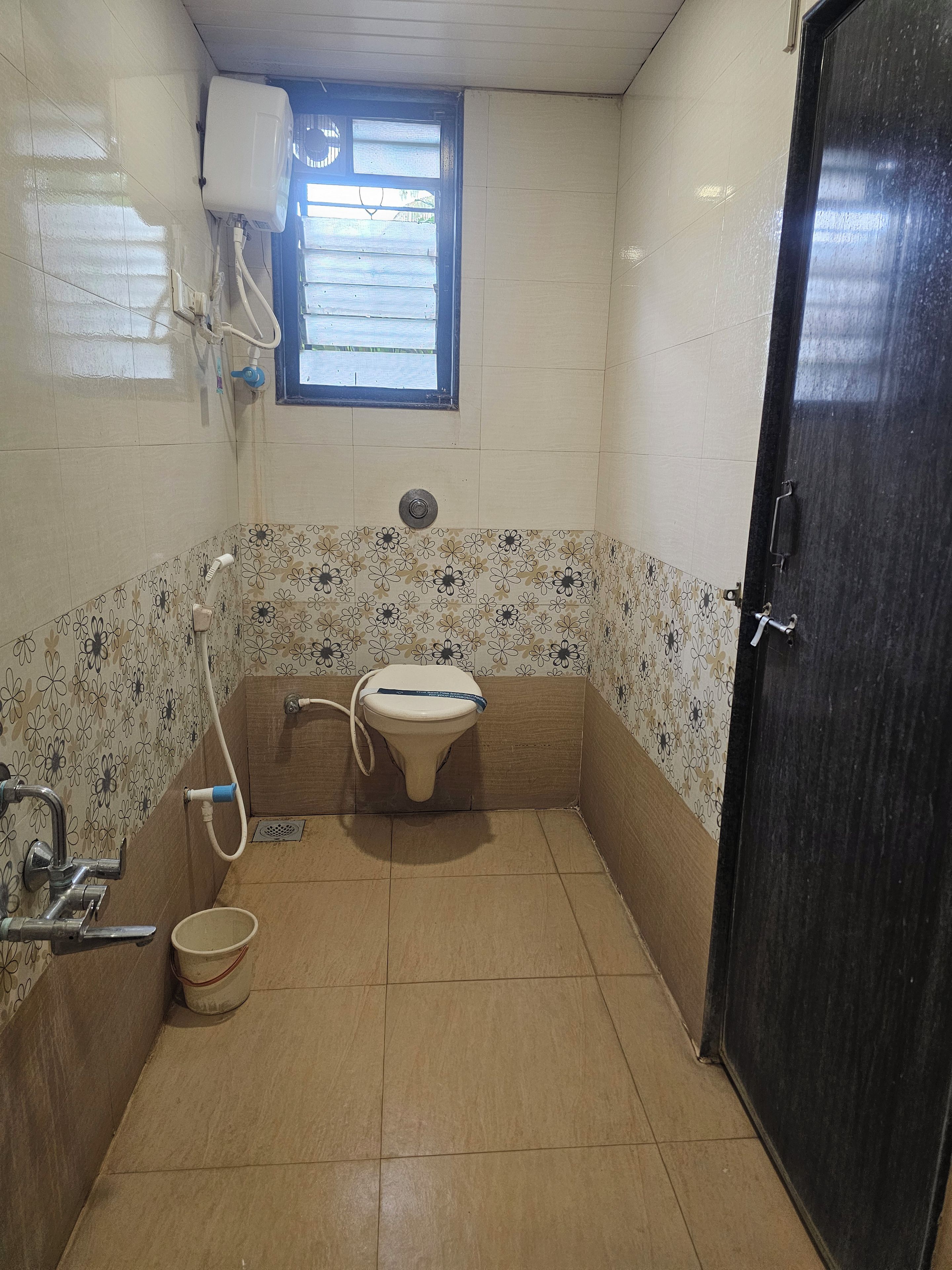 A small bathroom with a toilet, a bucket, a window, and a door.