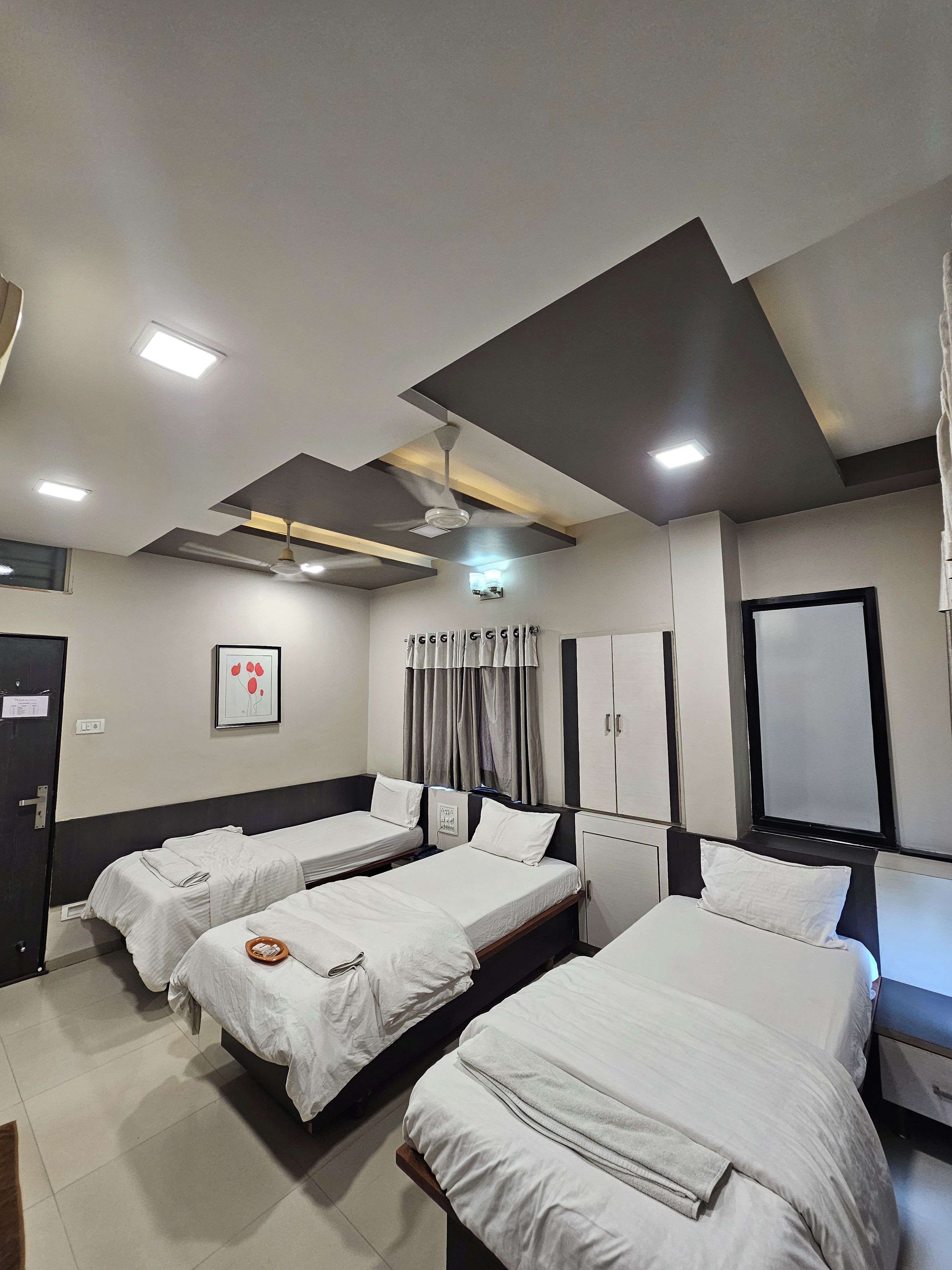 A hotel room with three beds, a ceiling fan, a flat-screen TV, and a framed picture on the wall.