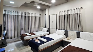 A hotel room with two beds, a desk, a chair, a TV, and a ceiling fan.