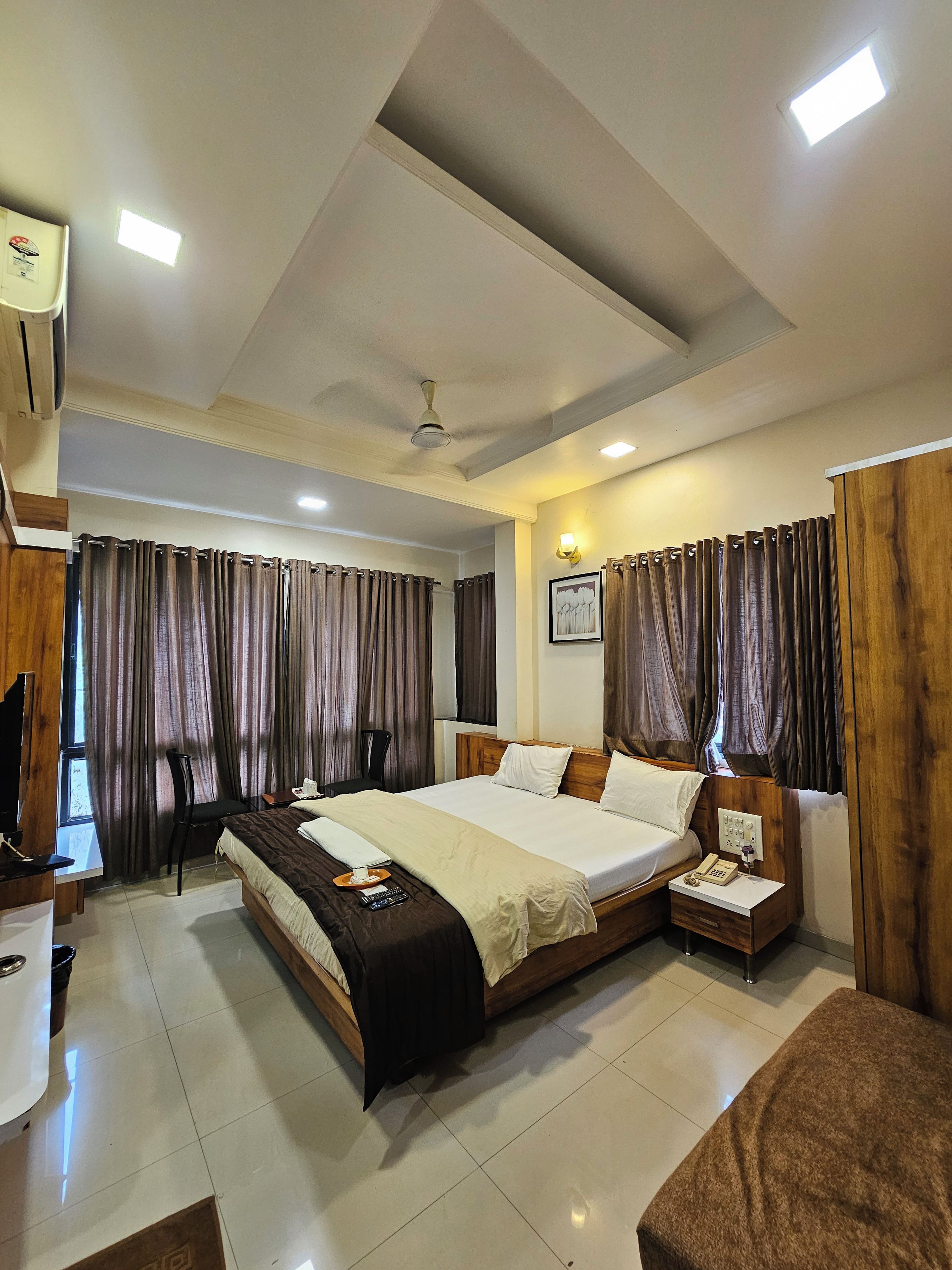 A hotel room with a large bed, a desk with a chair, a bedside table with a lamp, and a ceiling fan.