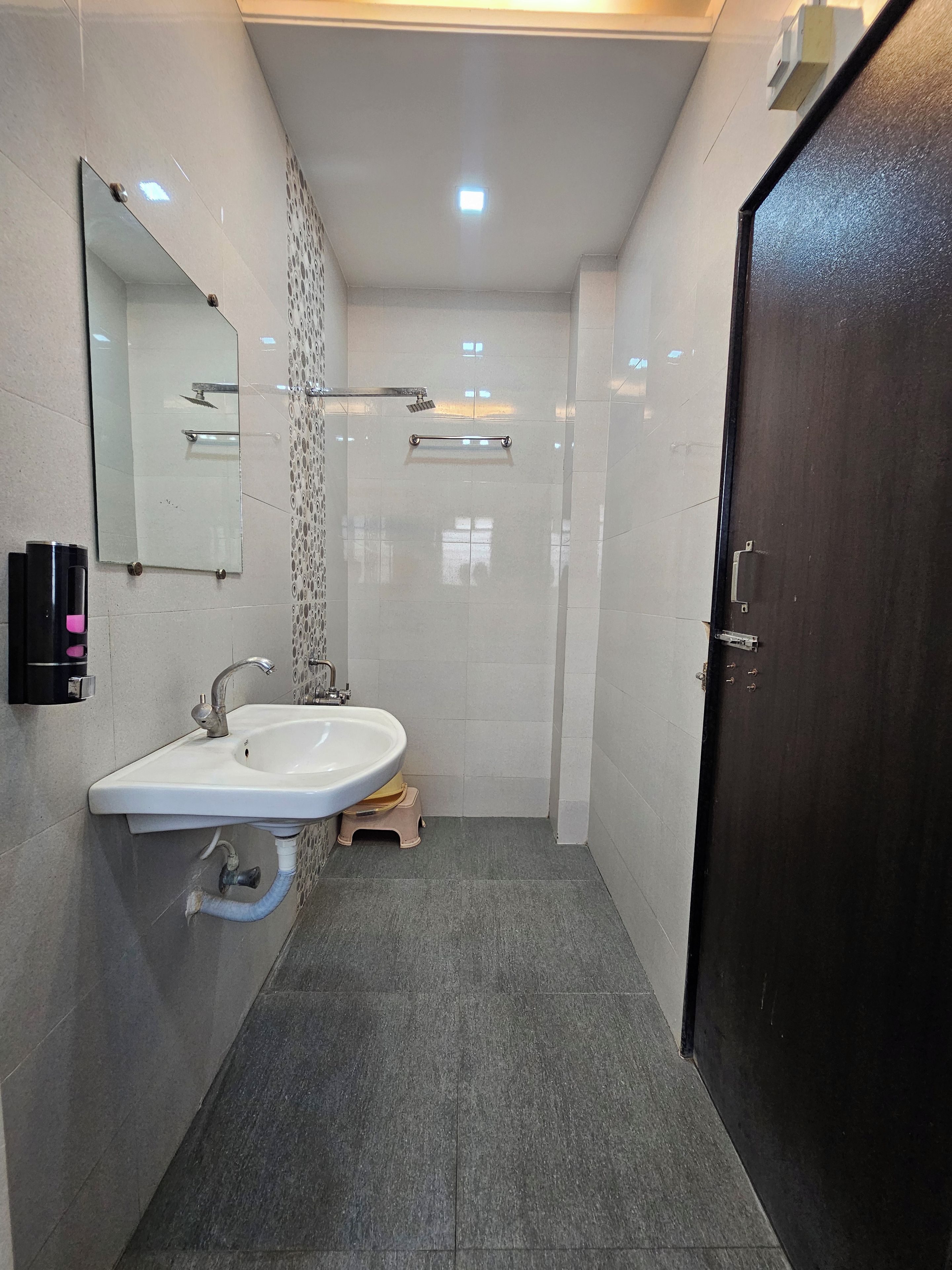 A modern bathroom with a white sink, a mirror, a shower, and a dark door.