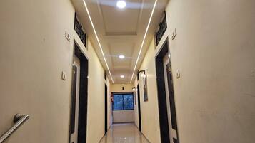 A hallway with a modern design, featuring a long corridor with doors on either side, a tiled floor, and recessed lighting on the ceiling.