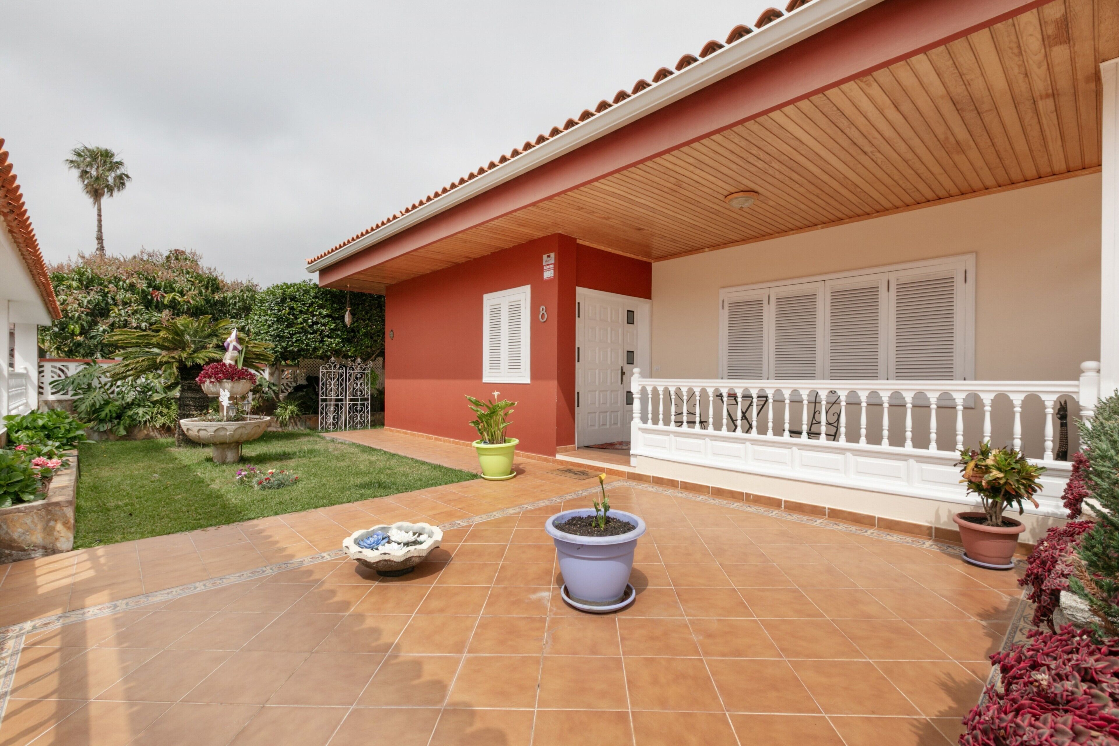 A courtyard with a tiled floor, potted plants, a small fountain, and a white railing.