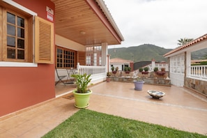 Une terrasse couverte agrémentée de plantes en pot, une clôture blanche et une vue sur une colline.