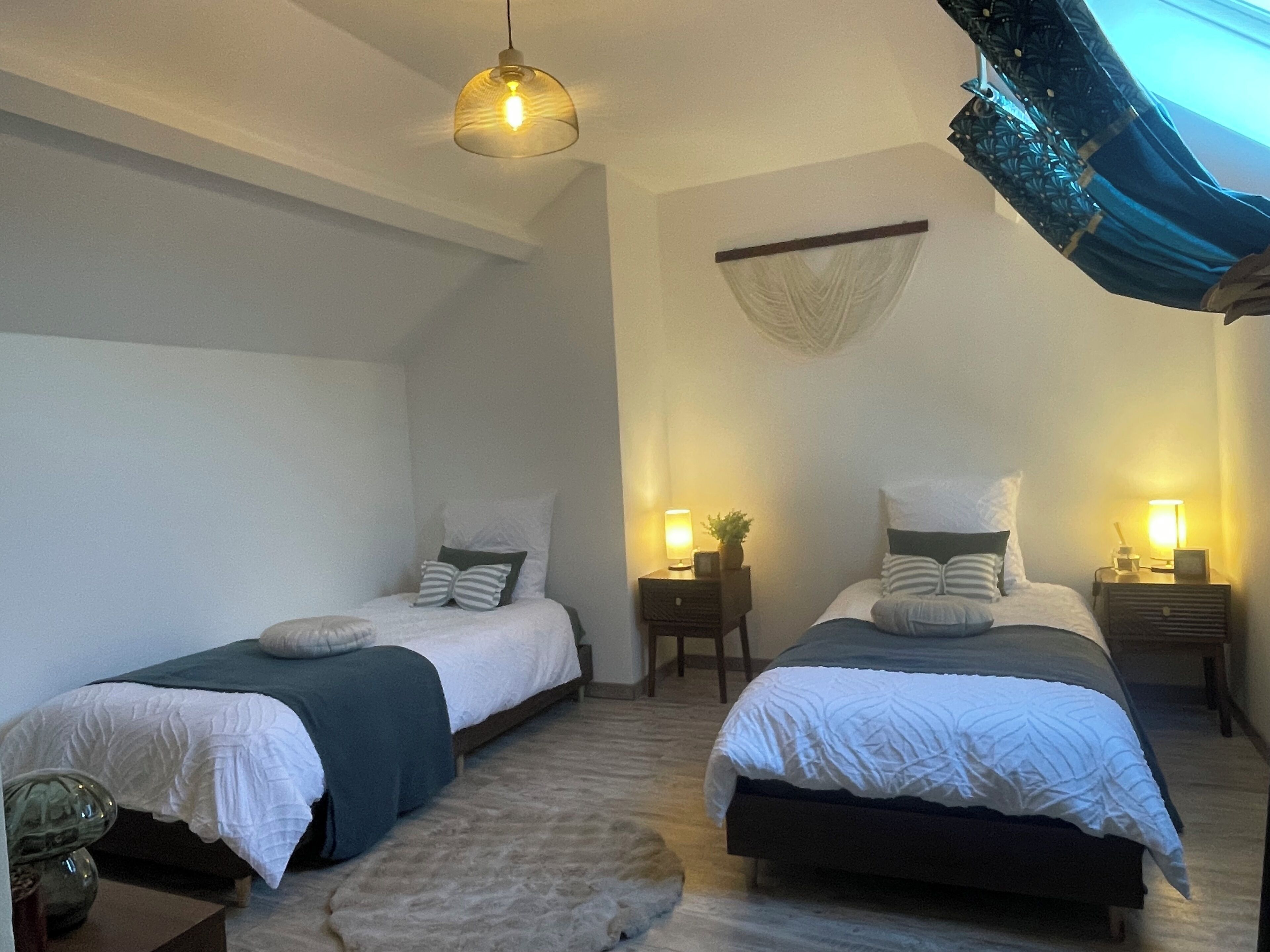 A bedroom with two beds, bedside lamps, a hanging light fixture, and a decorative wall hanging.