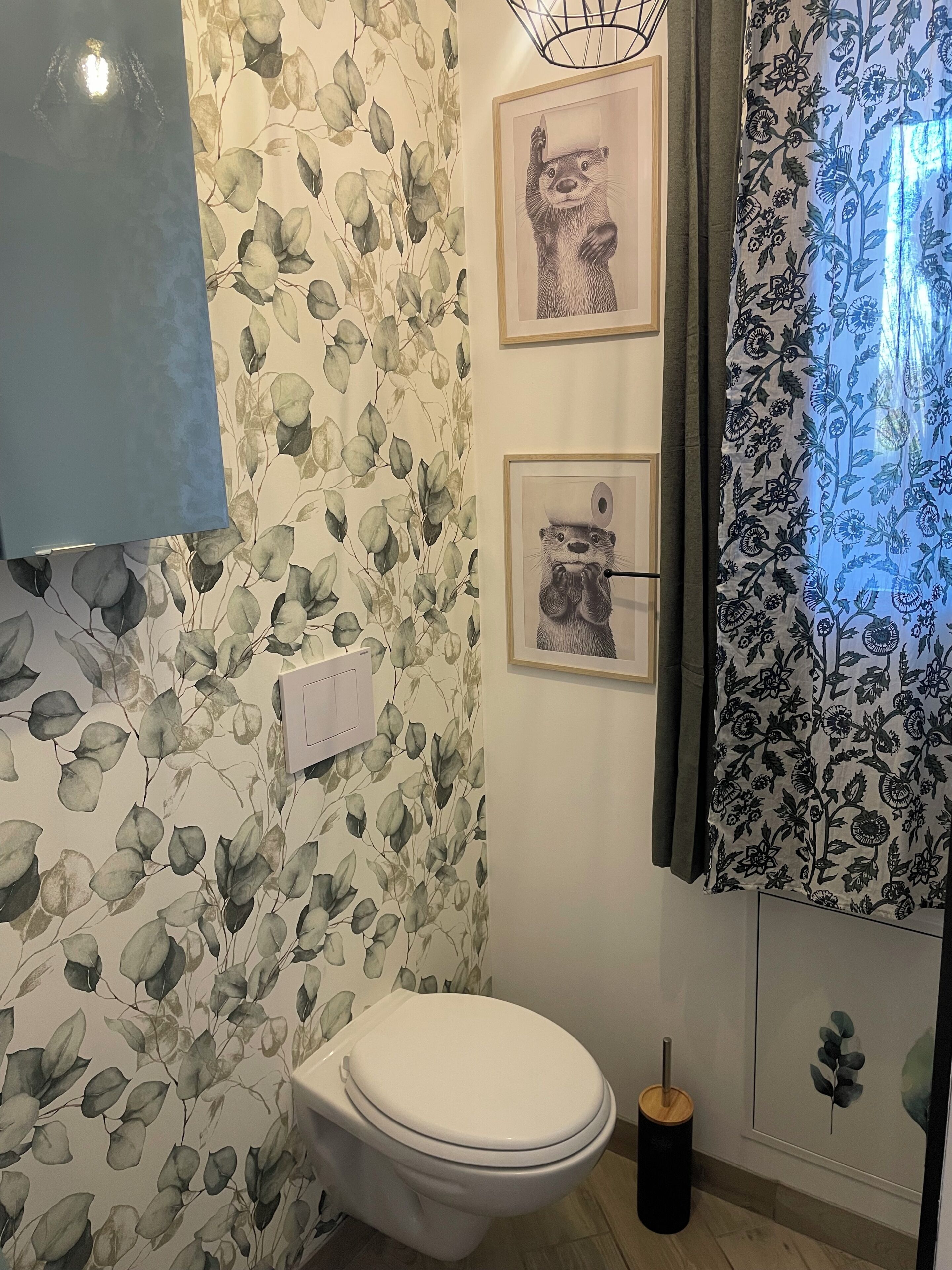 Kylpyhuone, jossa on wc, seinään kiinnitetty valaisin ja kehystetty taideteos.