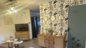 A living room with a TV, wooden cabinet, and a door with a floral pattern. - Le Gîte des Romains Country house (Anor)
