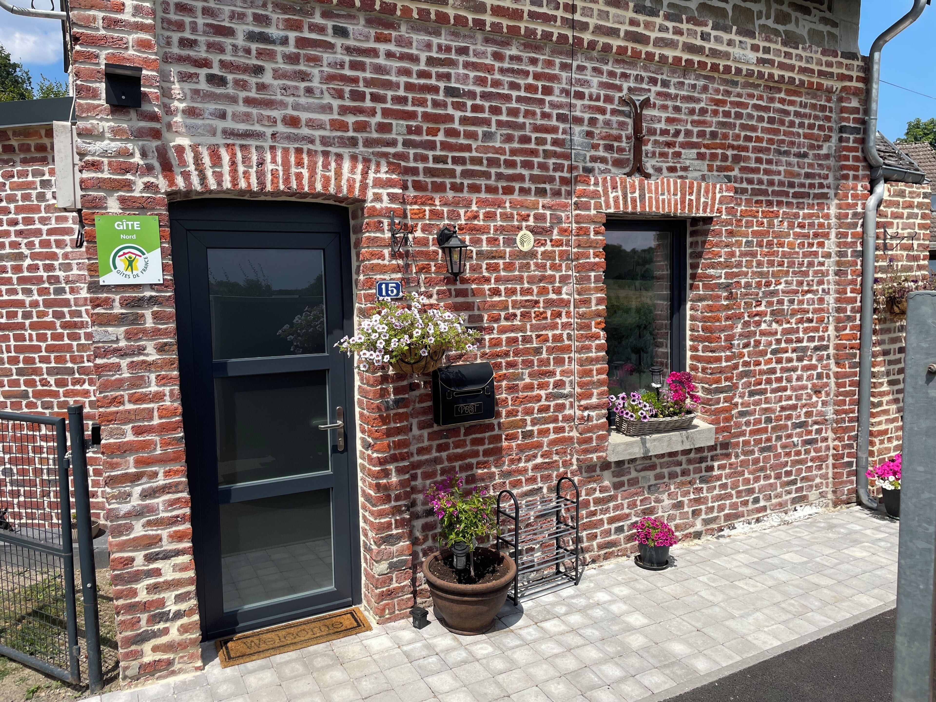 Ein Backsteinhaus mit einer schwarzen Tür, einem Briefkasten und Blumenkästen an den Fensterbänken.