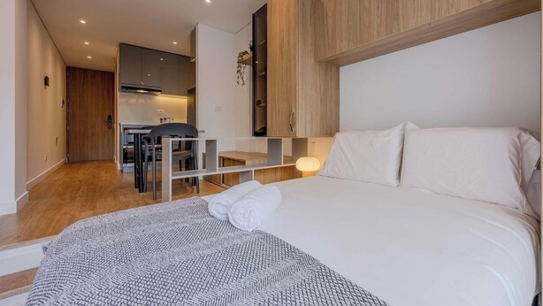 Et hotelværelse med seng, skrivebord og et tekøkken.