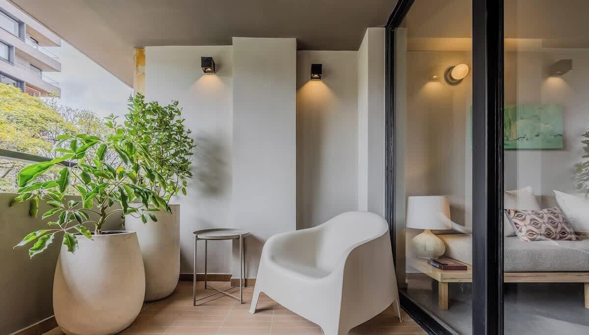 A modern living room with a white chair, a small table, and two large potted plants.