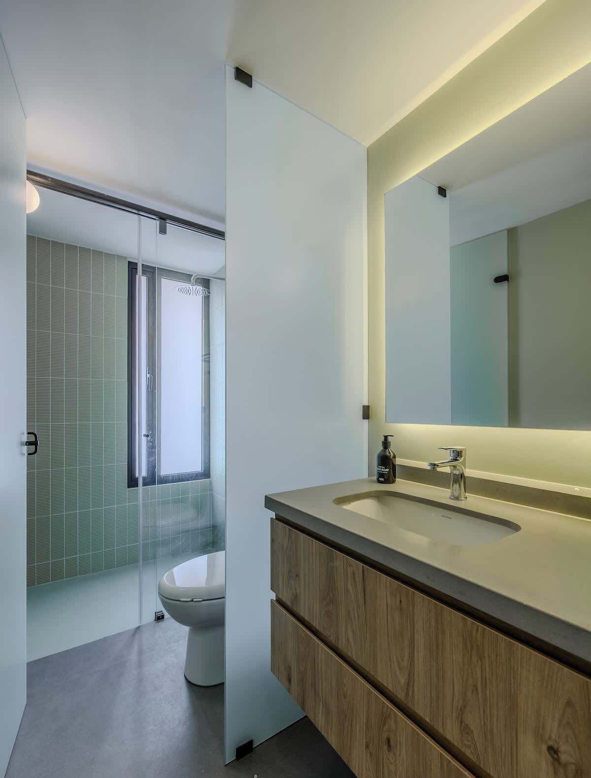 A modern bathroom with a glass shower enclosure, a toilet, and a vanity with a large mirror.