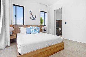A bedroom with a wooden bed, white bedding, a wall anchor decoration, and a view of the outdoors. - NOK Luxury 1BR Apartment, The Towers by Vistacana (Punta Cana)