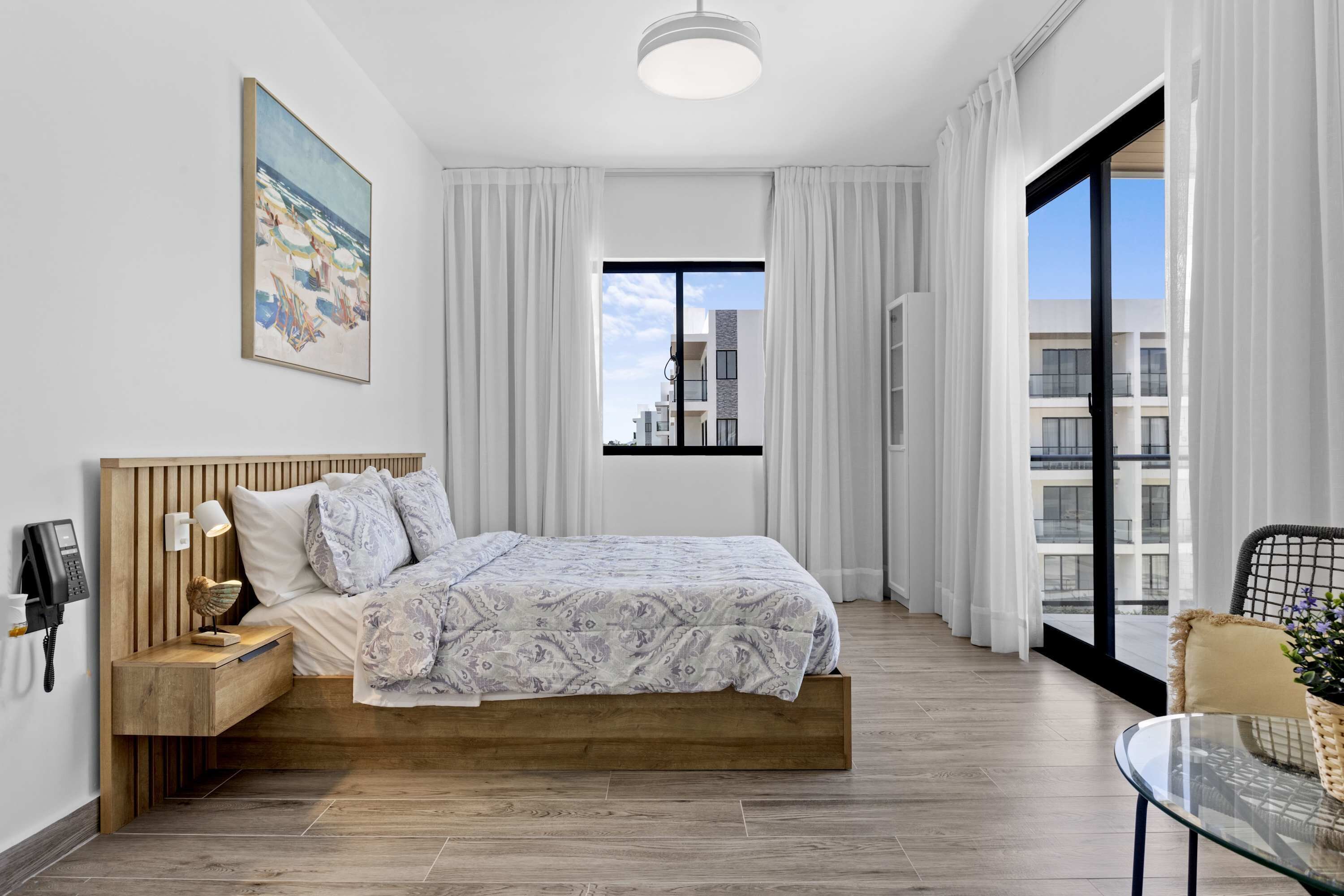 Une chambre d’hôtel moderne, équipée d’un lit, d’une table de chevet, d’une lampe et offrant une vue sur la ville grâce à une grande fenêtre.