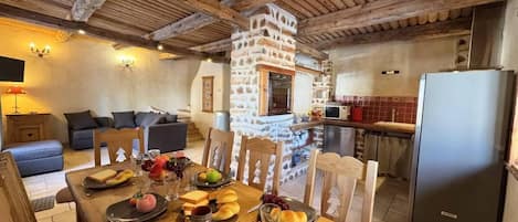 A cozy dining area with a stone fireplace, wooden furniture, and a modern kitchen in the background.