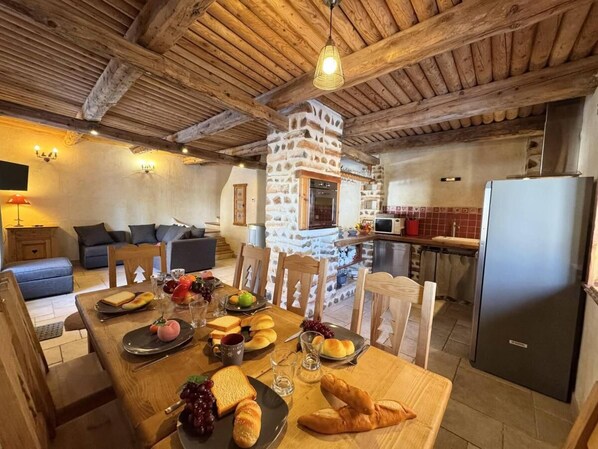 Ein gemütlicher Essbereich mit Kamin aus Stein, Holzmöbeln und einer modernen Küche im Hintergrund.