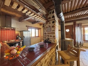 Eine rustikale Küche mit Steinwand, Holzbalken und einem Holztisch mit Stühlen.