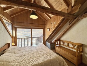 Ein Schlafzimmer mit Holzboden, einem Bett, einer Bank und einem Balkon mit Geländer.
