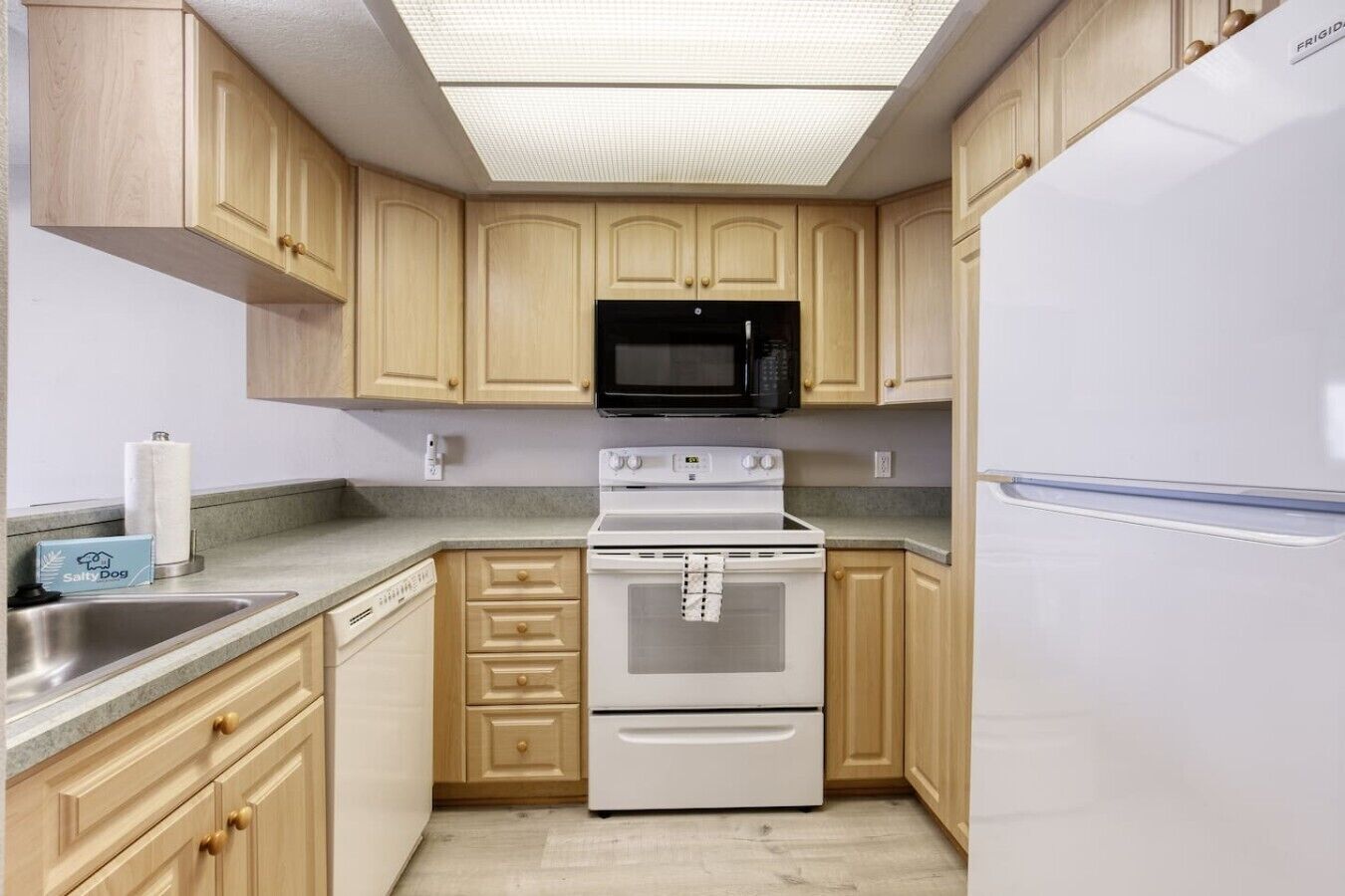 A kitchen with wooden cabinets, a white refrigerator, a microwave, a stove, and a dishwasher.