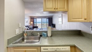 A kitchenette with a sink, a dish soap dispenser, and a dish rack. There is a dining area with a table and chairs, and a view of the ocean. - Ormond Beach, Ocean View, Balcony, Beach Access (Ormond Beach)