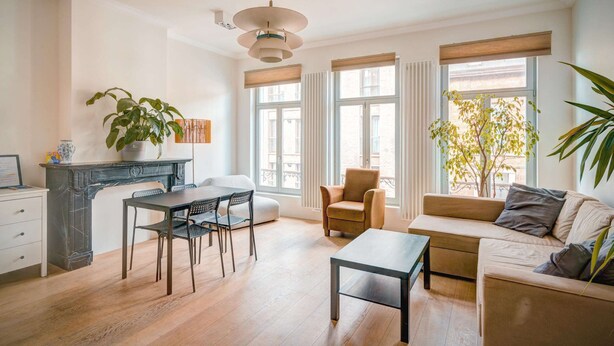 Una sala de estar moderna con una mesa de comedor, sofá y sillas, una chimenea y ventanas grandes.