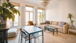Una sala de estar moderna con un sofá, una mesa de comedor, sillas y ventanas amplias.