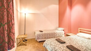 Une chambre avec deux lits, une table de chevet, une lampe et un rideau à motifs.