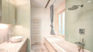 Une salle de bain moderne dotée d’une grande baignoire, d’une douche séparée, d’un meuble-lavabo avec un vasque et d’une serviette accrochée au mur.