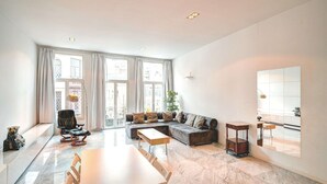 Un salon spacieux avec une grande fenêtre, un canapé, une table à manger et une petite table d’appoint.