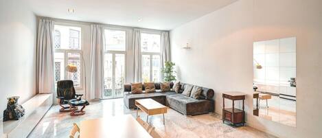 A spacious living room with a large window, a sofa, a dining table, and a small side table.