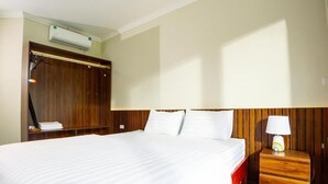 Ein Hotelzimmer mit einem großen Bett, einem Holz-Kopfschild, einem Nachttisch mit Lampe und einer Wand-Klimaanlage.