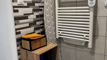 A bathroom with a patterned wall, a towel rack, a radiator, and a wooden shelf with a yellow towel.